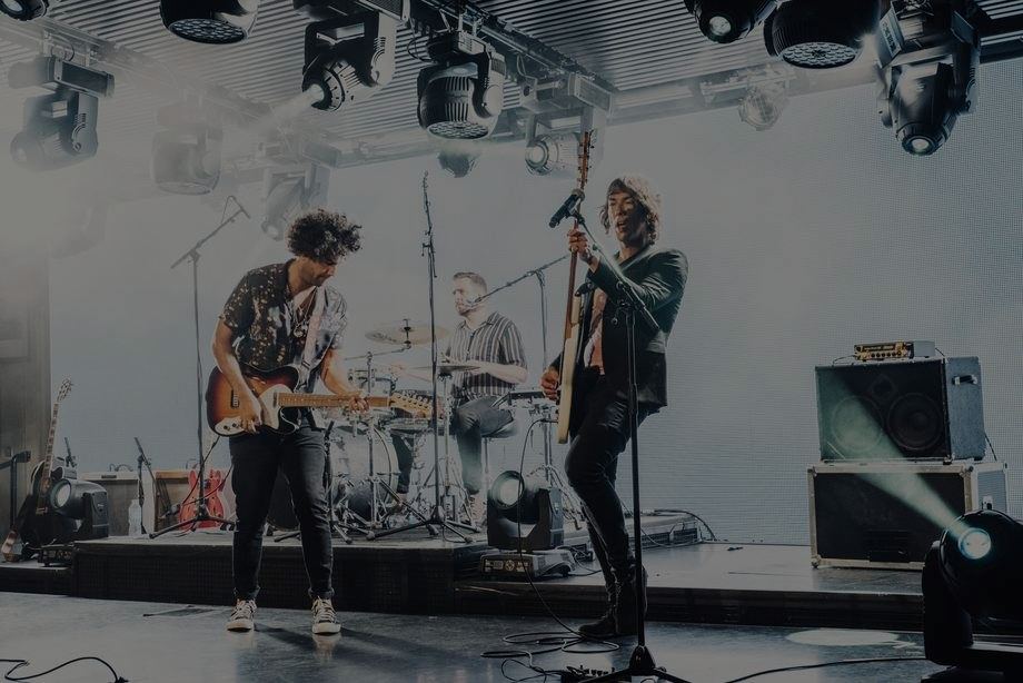 The band on a white stage with guitars and drums under moving lights