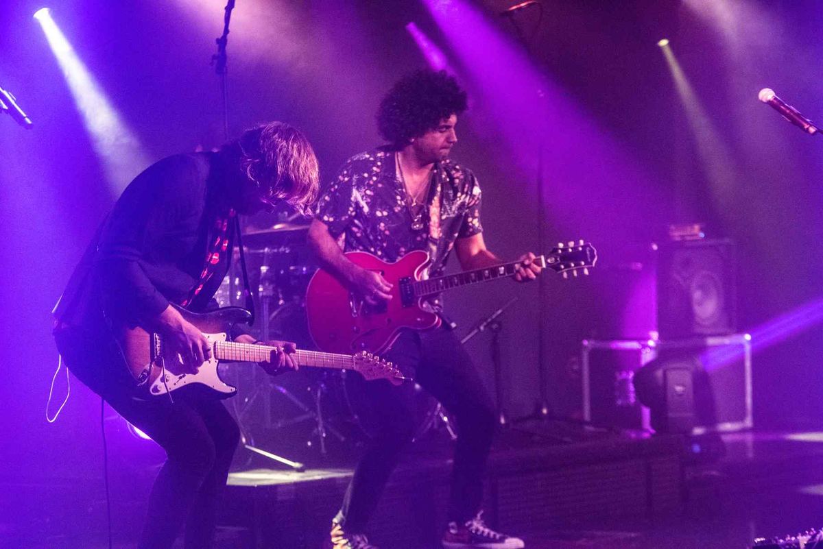 Two West Coast Heroes guitarists playing together under purple stage lights
